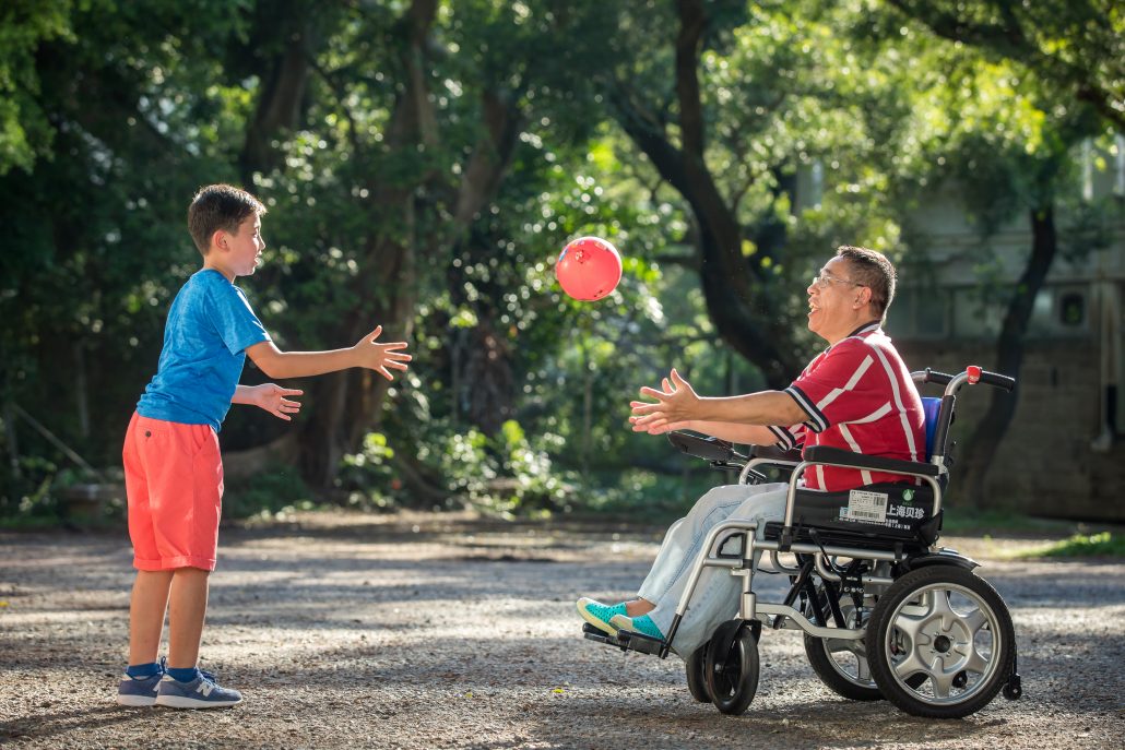 A kid throw a ball to a man in armchair A kid throw a ball to a man in armchair